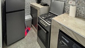 Une cuisine compacte équipée d’un réfrigérateur, d’une cuisinière, d’un four et d’un four à micro-ondes. On peut voir des bouteilles d’eau sur le comptoir, et un panier est suspendu au plafond.