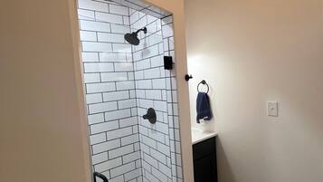 Une salle de bain avec un espace douche agrémenté de carreaux de céramique blanche imitant des briques, un porte-serviettes noir et un carrelage au motif décoratif.