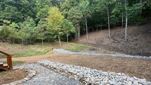 A gravel path leading through a wooded area with a wooden bench and a stone wall.