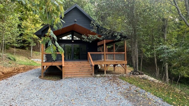A cabin with a wooden deck, a covered porch, and a gravel driveway.