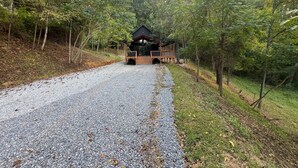 A cabin with a gravel driveway leading to a wooden deck and a covered porch.