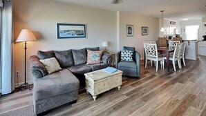 A living room with a sofa, ottoman, and a dining area with chairs and a table.