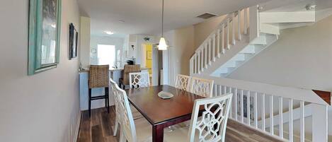 A dining area with a wooden table and white chairs, a staircase with white railings, and a hanging light fixture.