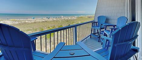 Une terrasse avec des chaises Adirondack bleues et une table donnant sur une plage.