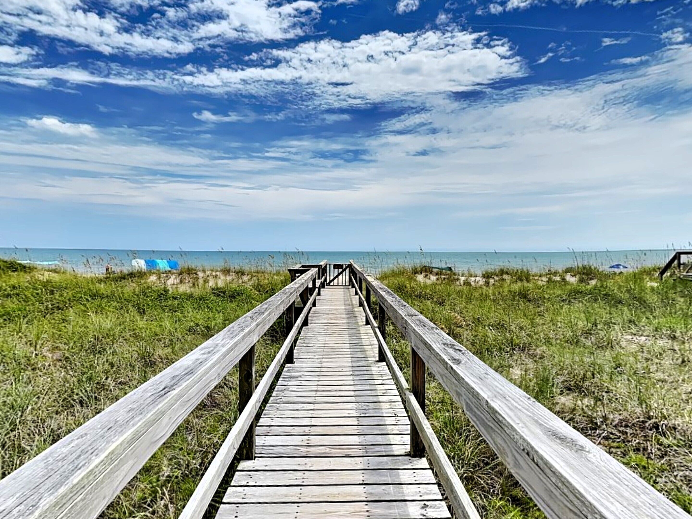 Una passerella di legno che conduce a una spiaggia sotto un cielo sereno.