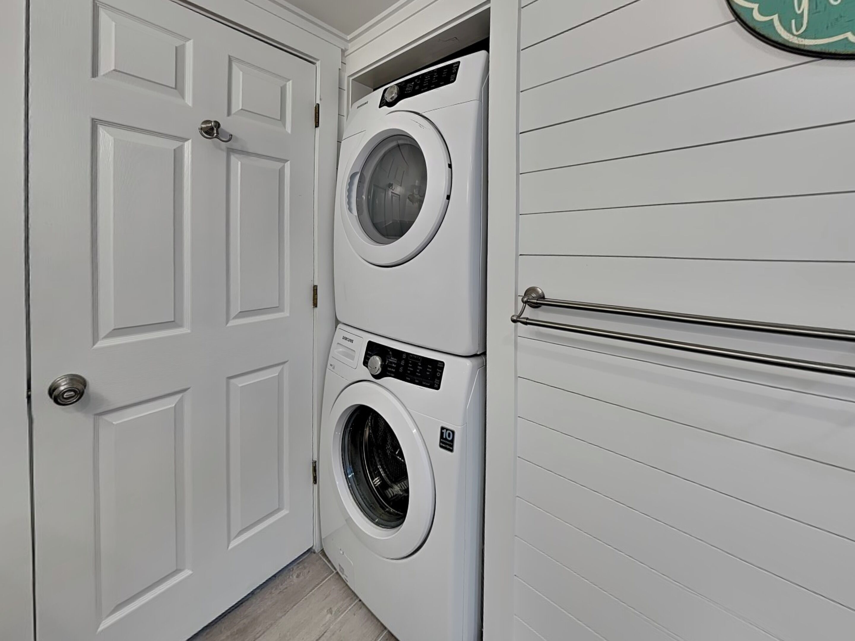 A laundry room with two stacked front-loading washing machines, a white door, and a towel rack.