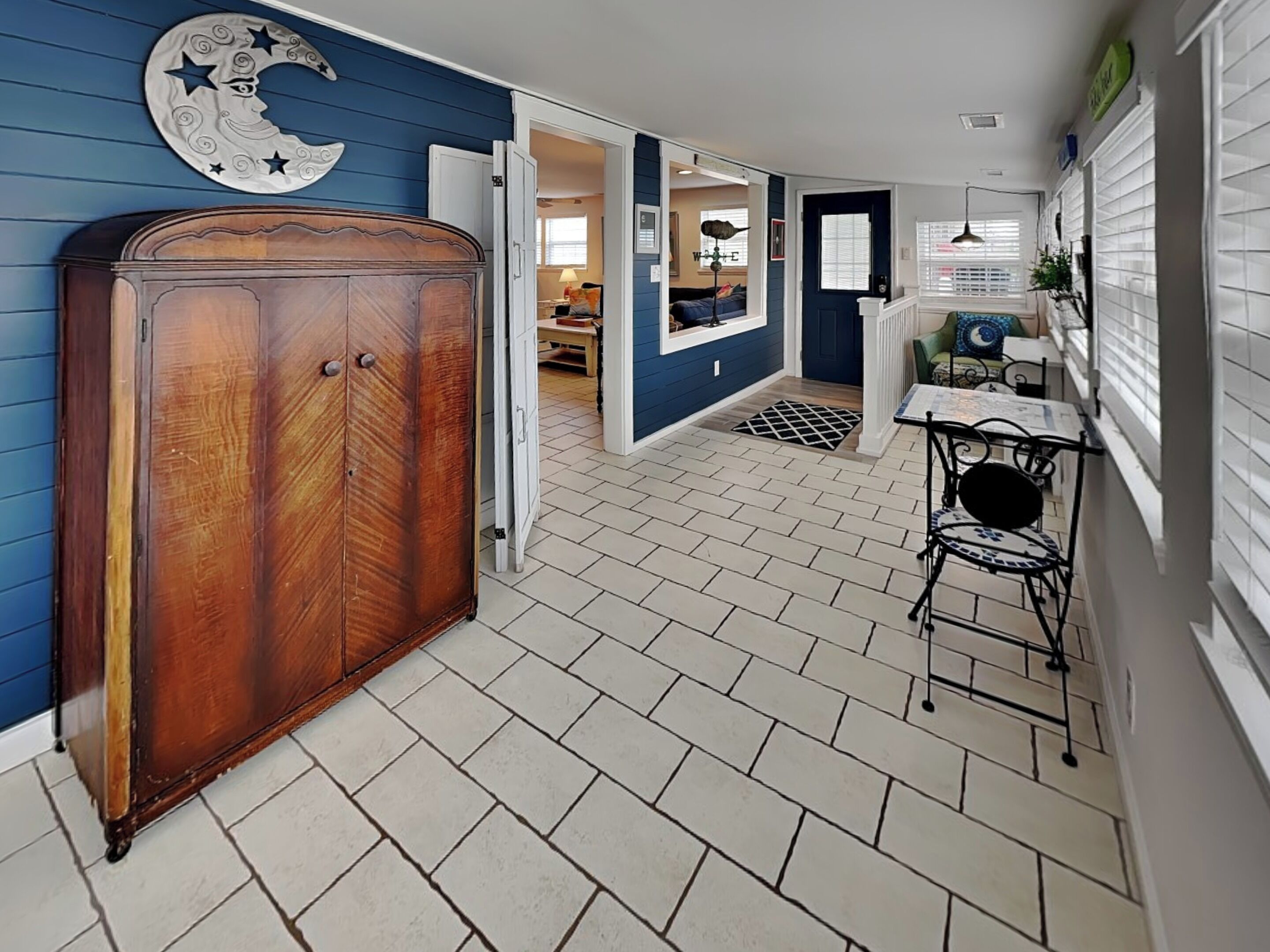 A hallway with a wooden wardrobe, a small table with chairs, and a decorative moon and stars wall piece.