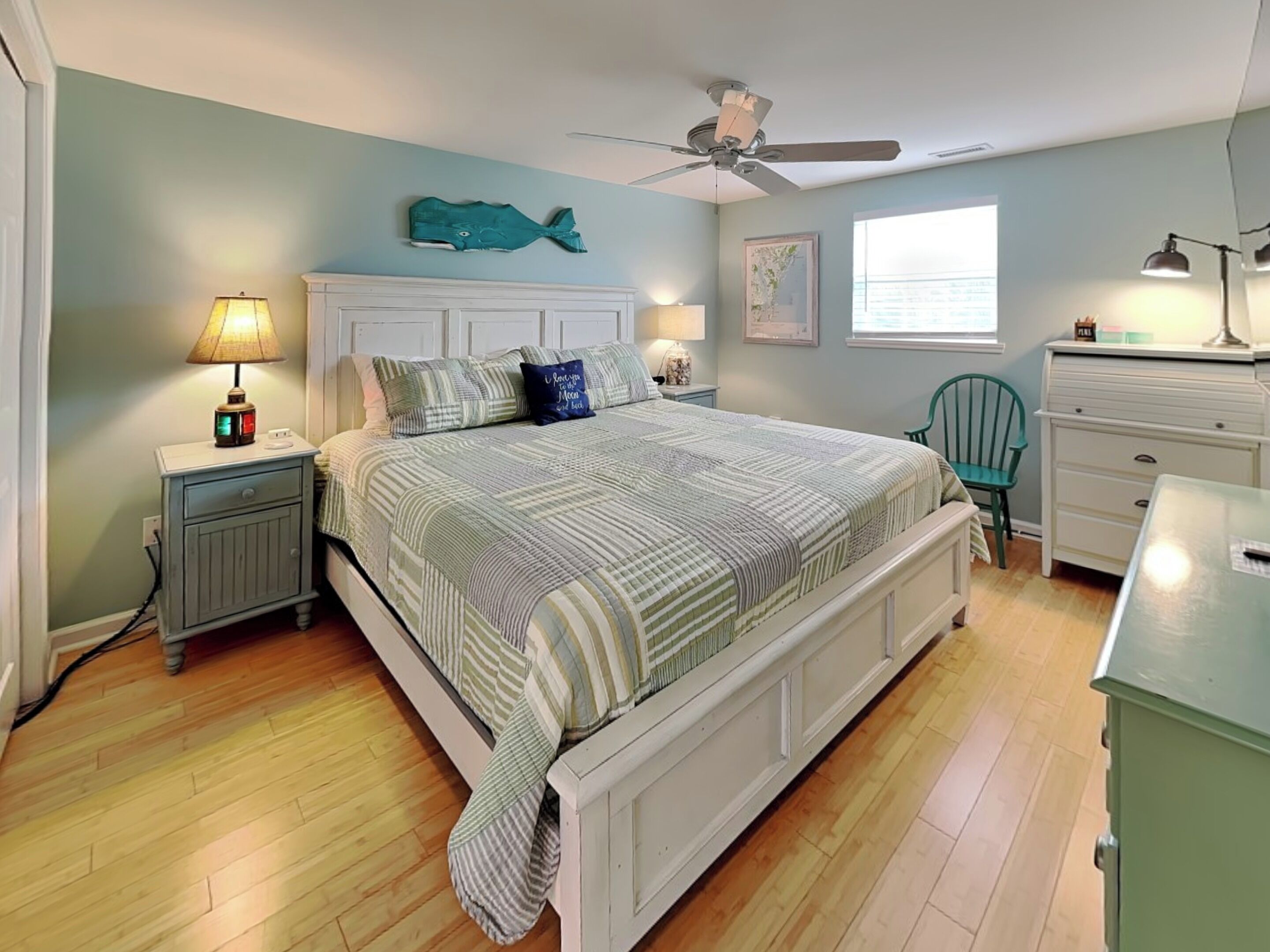 Un dormitorio con cama, mesitas de noche, cómoda, silla y ventilador de techo.