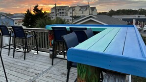 A wooden deck with blue and green chairs, overlooking a residential area with houses and a clear sky. - Silvery Moon by Carolina Retreats (Carolina Beach)