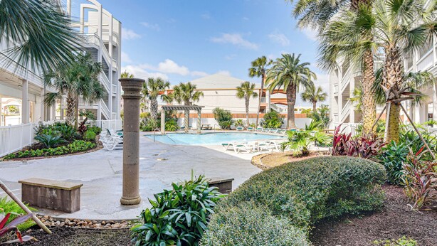 Un espace piscine doté de chaises longues, de palmiers et d’un bâtiment avec des balcons.