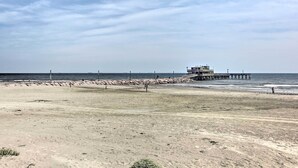Une plage avec une jetée qui s’avance dans l’océan, et un bâtiment à son extrémité.