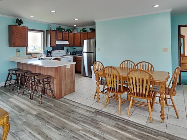 A spacious kitchen with a central island, wooden dining table, and bar stools. - Hoff 1 by Topsail Realty (Holly Ridge)