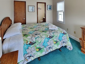 Un dormitorio con una cama, cabecera de madera, una puerta, una ventana y un aparador.