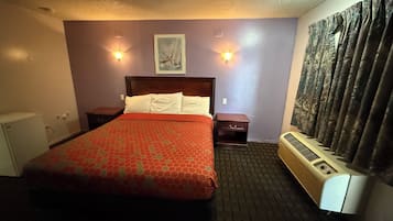 A hotel room with a bed, two bedside tables, a heater, a wall-mounted picture, and a window with curtains.