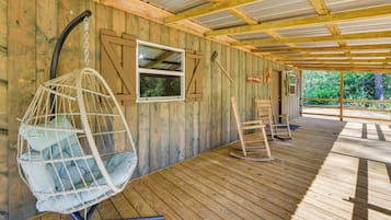 A wooden deck with a hanging chair, a wooden bench, and a window.
