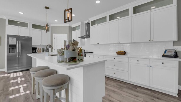 A modern kitchen with white cabinetry, a central island with stools, and pendant lighting. - River’s Bend Sanctuary- WALK to Beach & Downtown (Caseville)