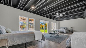 A modern bedroom with two beds, a dining table, and a large window with a view of a garden. - River’s Bend Sanctuary- WALK to Beach & Downtown (Caseville)
