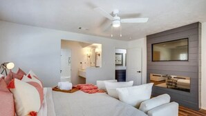 A modern hotel room with a bed, a seating area, a TV, and a ceiling fan. - Retreat @ The One | Movie Theater | Coffee Bar (Conroe)