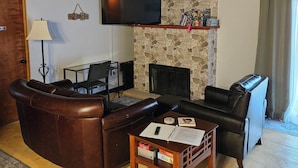 A living room with a stone fireplace, leather sofas, a flat-screen TV, and a coffee table. - Rustic-Chic 2 bdr Pet Friendly Log Cabin, Steps to Lake Huron (Au Gres)
