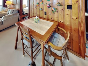 A wooden dining table with a placemat, surrounded by four wooden chairs with cushioned seats. - Pana-Sea-A by Topsail Realty (Holly Ridge)