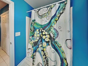 Ein Badezimmer mit blauer Wand, weißer Tür und einer Duschvorhang mit einem farbenfrohen, abstrakten Muster.