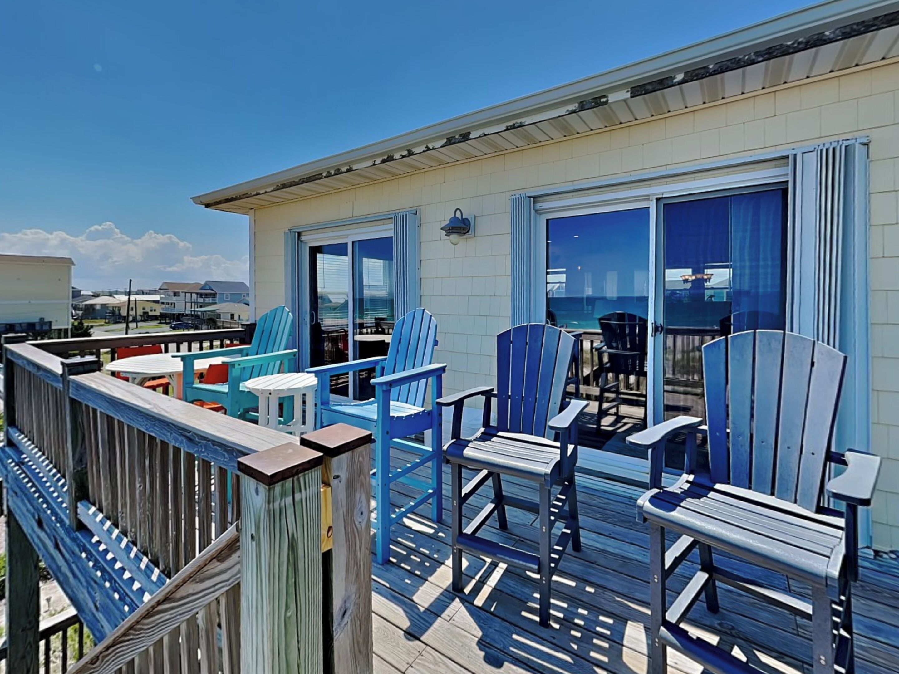 A deck with blue Adirondack chairs, a wooden table, and a glass door leading to a balcony.