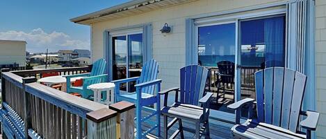 A deck with blue Adirondack chairs, a wooden table, and a glass door leading to a balcony.