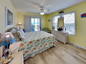 A bedroom with a bed, dresser, and a view of the beach through the window.