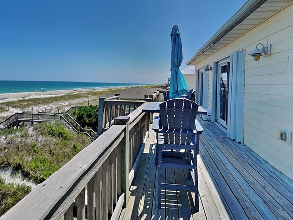 A wooden deck with a table and chairs overlooking a beach. - Piccolo Paradiso by Topsail Realty (Holly Ridge)
