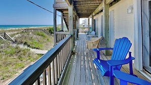 Un pontile di legno con vista sulla spiaggia, una zona riparata con sedie e un edificio con una finestra.