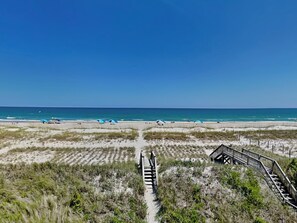 A beach with a wooden boardwalk leading to the water, surrounded by dunes and sparse vegetation. - Piccolo Paradiso by Topsail Realty (Holly Ridge)