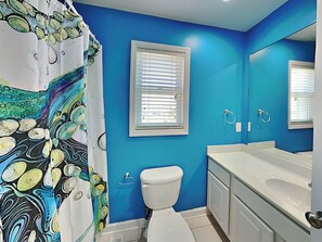 A bathroom with a blue wall, a white toilet, a white sink, and a shower curtain with a colorful pattern.