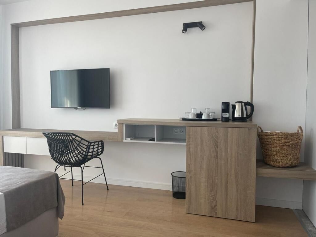 Habitació moderna amb televisió de pantalla plana penjada a la paret, escriptori de fusta amb una cafetera, cistella de vímet i cadira negra.