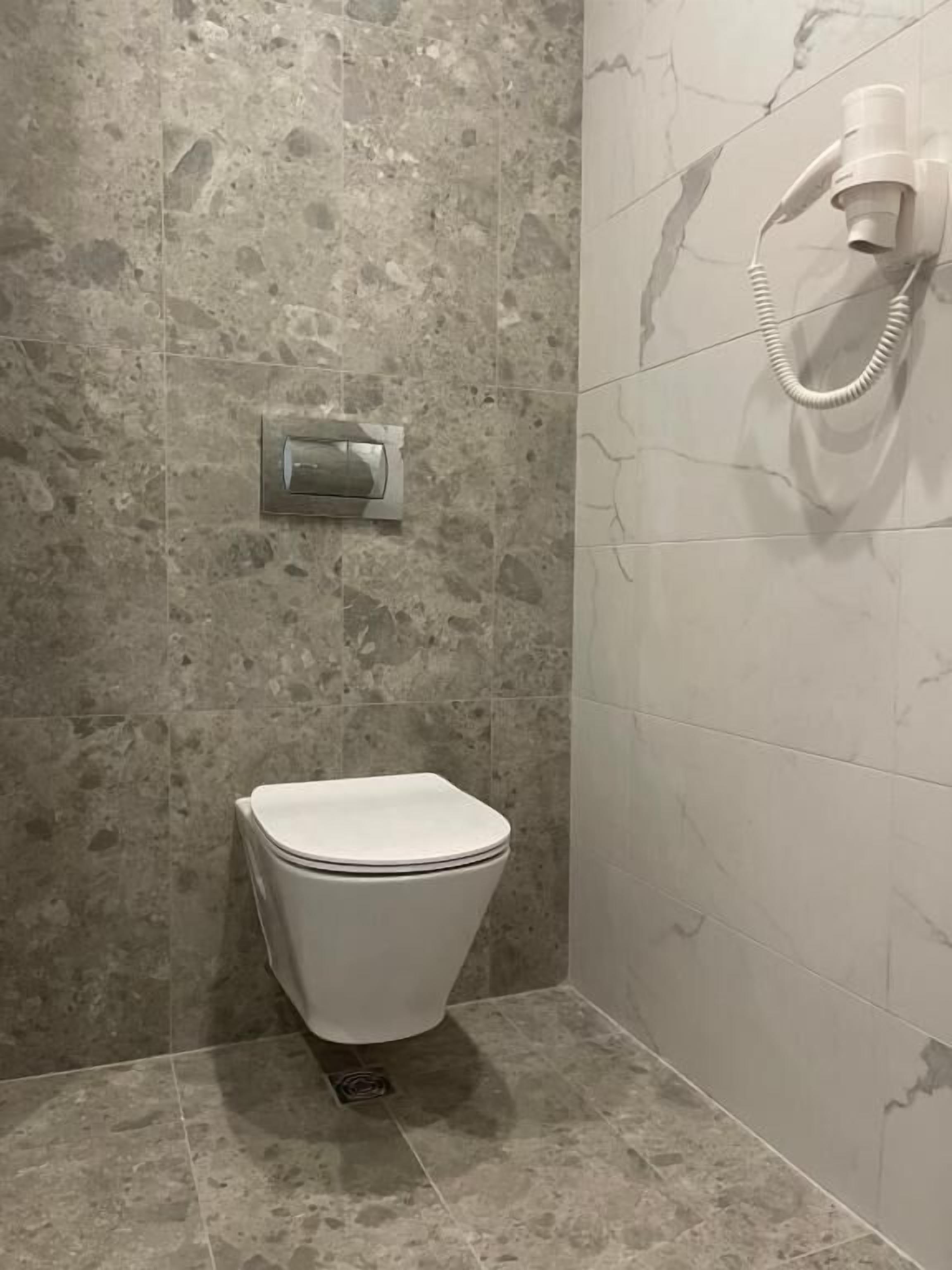 Egy fürdőszoba, amelyben WC, zuhanyzó és a falra szerelt fűtőtest található.