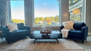 A living room with two sofas, a coffee table, and a large window with a view of trees.