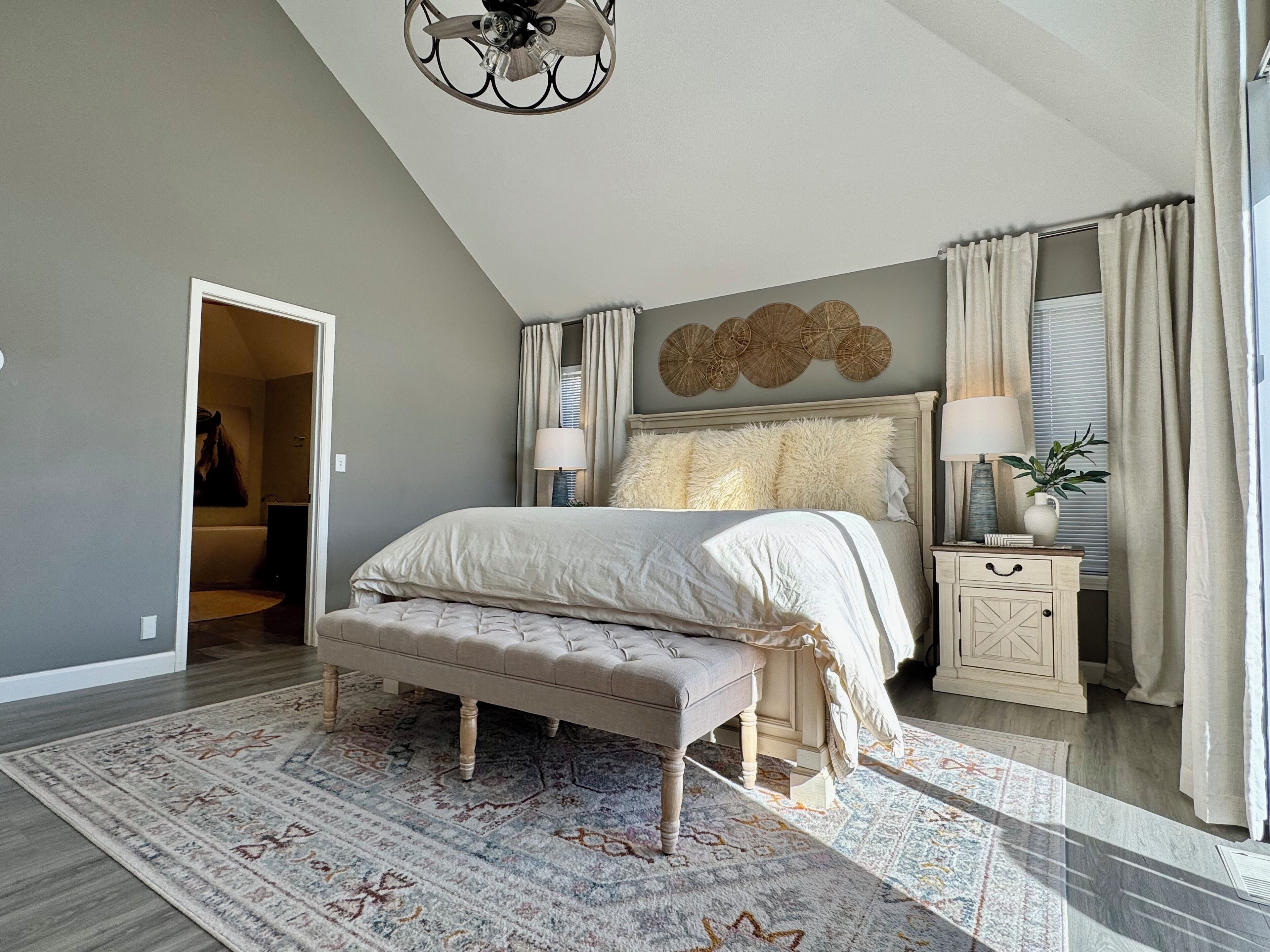 A bedroom with a large bed, a bench, a bedside table, a lamp, and a wall decoration.