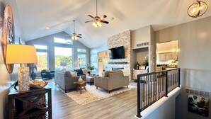 A spacious living area with a fireplace, a kitchen with white cabinets, and a staircase with a black railing.