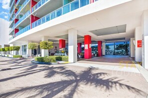 A modern hotel entrance with a covered walkway, red pillars, and neatly trimmed bushes.