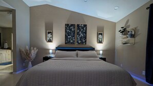 Une chambre avec un grand lit, deux tables de chevet et des étagères fixées au mur.