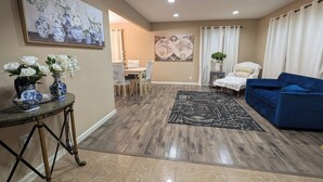 Un salon avec un canapé bleu, une table à manger avec des chaises, une table basse et un tableau accroché au mur.