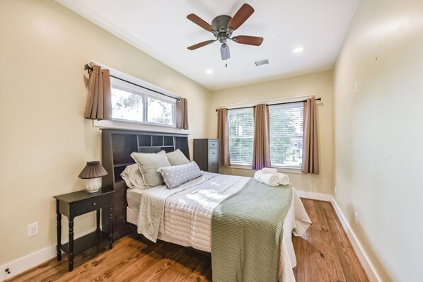 Une chambre à coucher avec un lit, une table de chevet, un ventilateur de plafond et des fenêtres.