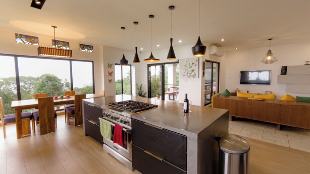 Una cocina moderna con una isla central, iluminación colgante y un comedor con vistas.