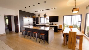 Una cocina moderna con una isla central, taburetes de bar, una mesa de comedor y un ventanal que proporciona luz natural.