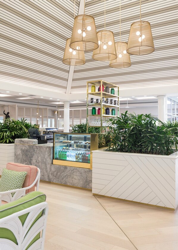A modern lobby with a high ceiling, a reception desk, a glass display case, and a variety of plants.