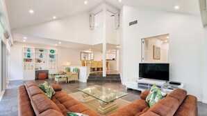 Un vaste espace de vie comprenant un canapé en cuir marron, une table basse en verre et un téléviseur à écran plat. Un escalier mène à un niveau supérieur, et un coin repas est aménagé avec des chaises et une table.