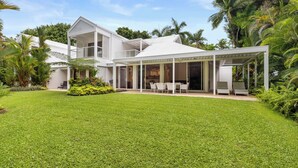 Une maison moderne dotée d’un patio couvert, d’une pelouse et d’une végétation tropicale.