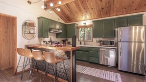 Une cuisine avec des meubles de rangement verts, un réfrigérateur en acier inoxydable, un four à micro-ondes et un coin bar avec des tabourets.