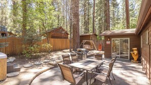 Une terrasse extérieure avec une table et des chaises, entourée d’une clôture en bois et d’arbres.
