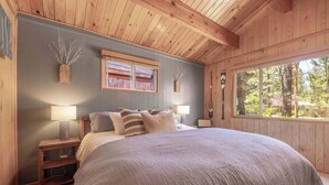 Une chambre avec un grand lit, deux tables de chevet, une fenêtre donnant sur des arbres et des murs en bois.