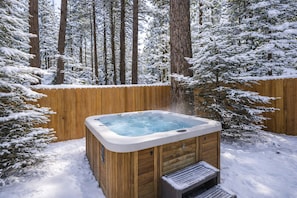 A wooden hot tub surrounded by snow-covered trees and a wooden fence. - Retro camp vibes meet modern comfort — hot tub under the stars, full game room, and walkable location near Summit & the Village. (Big Bear Lake)
